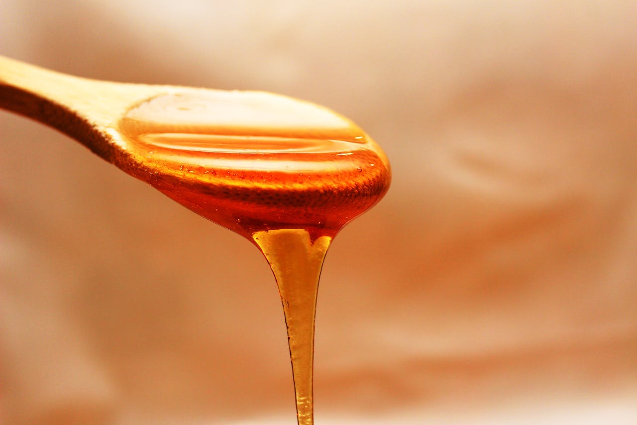 Close-up of honey dripping from a wooden spoon, showcasing its rich texture and color.